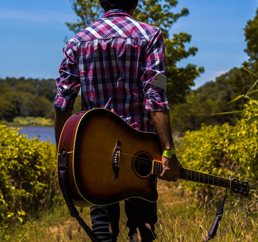 Back view of a man holding a guitar behind him as he walks