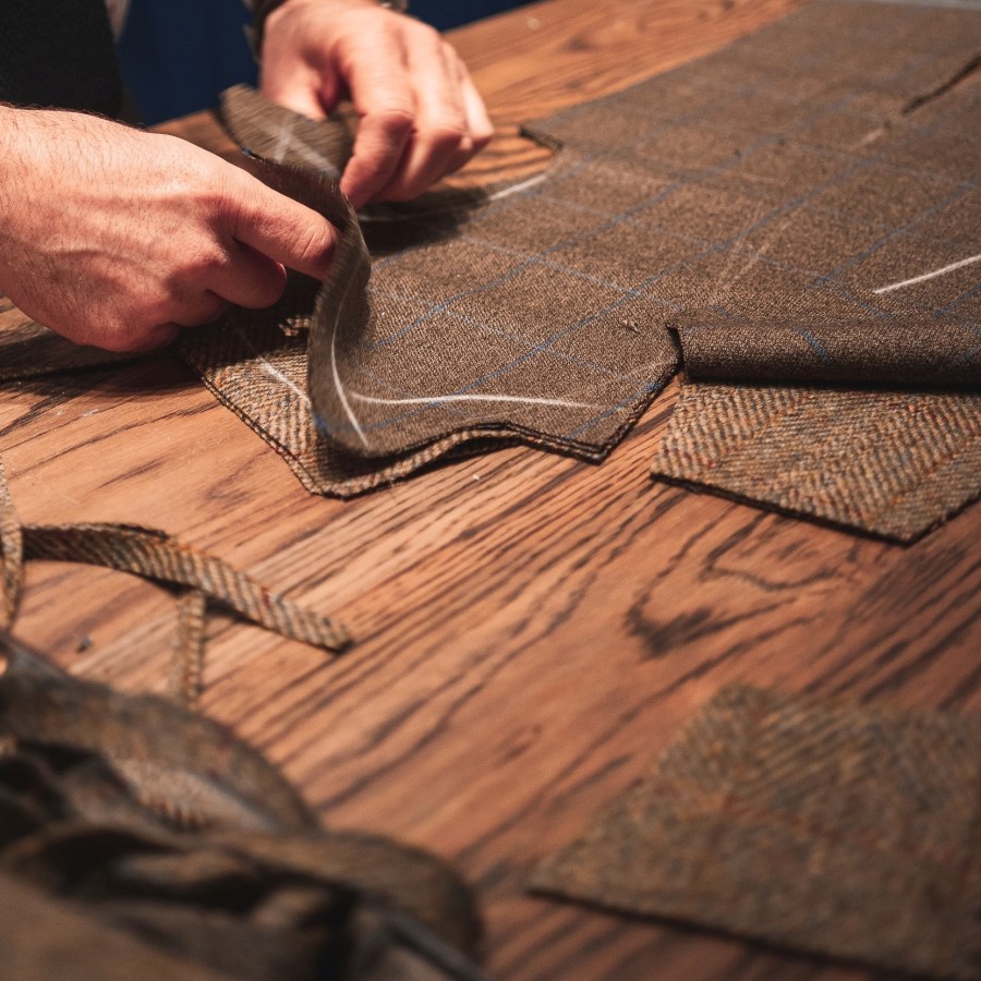 Hands sewing suit fabric on wooden table