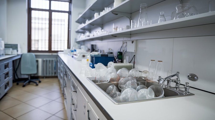 a sink in stark white counter on one side of a scientific laboratory, the sink is piled high with dirty beakers AI image
