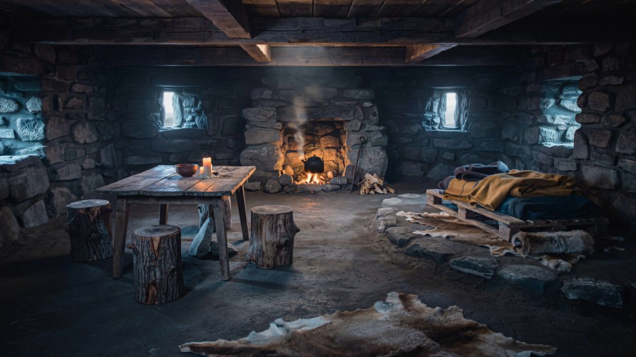 Cinematic fantasy photo of the inside of a square stone building with narrow windows, a battered old table, tree stumps for chairs and a pallet with blankets on a small platform in one corner. At the back is a cosy hearth with a warm fire and a tea kettle hanging over it, steam wafting from the spout Ideogram image